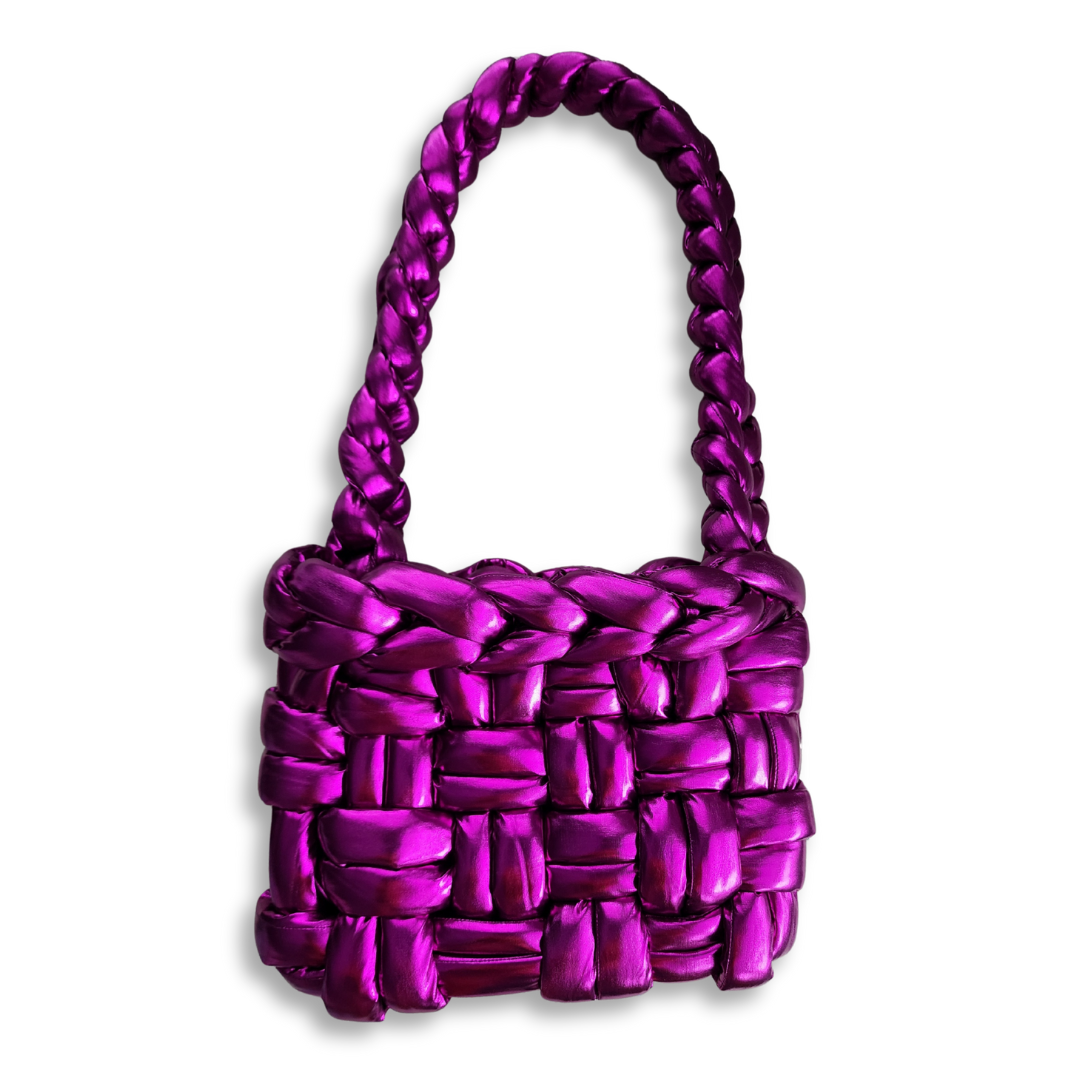 A handmade chunky knit handbag in shimmering metallic fuchsia, with a braided handle, standing upright against a white background.