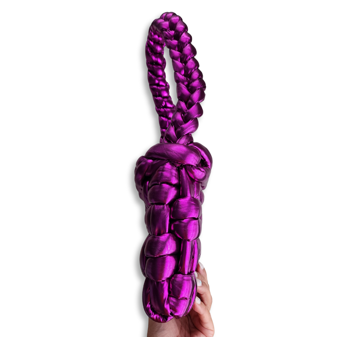 A handmade chunky knit handbag in shimmering metallic fuchsia, with a braided handle, held by a hand to show its side profile against a white background.