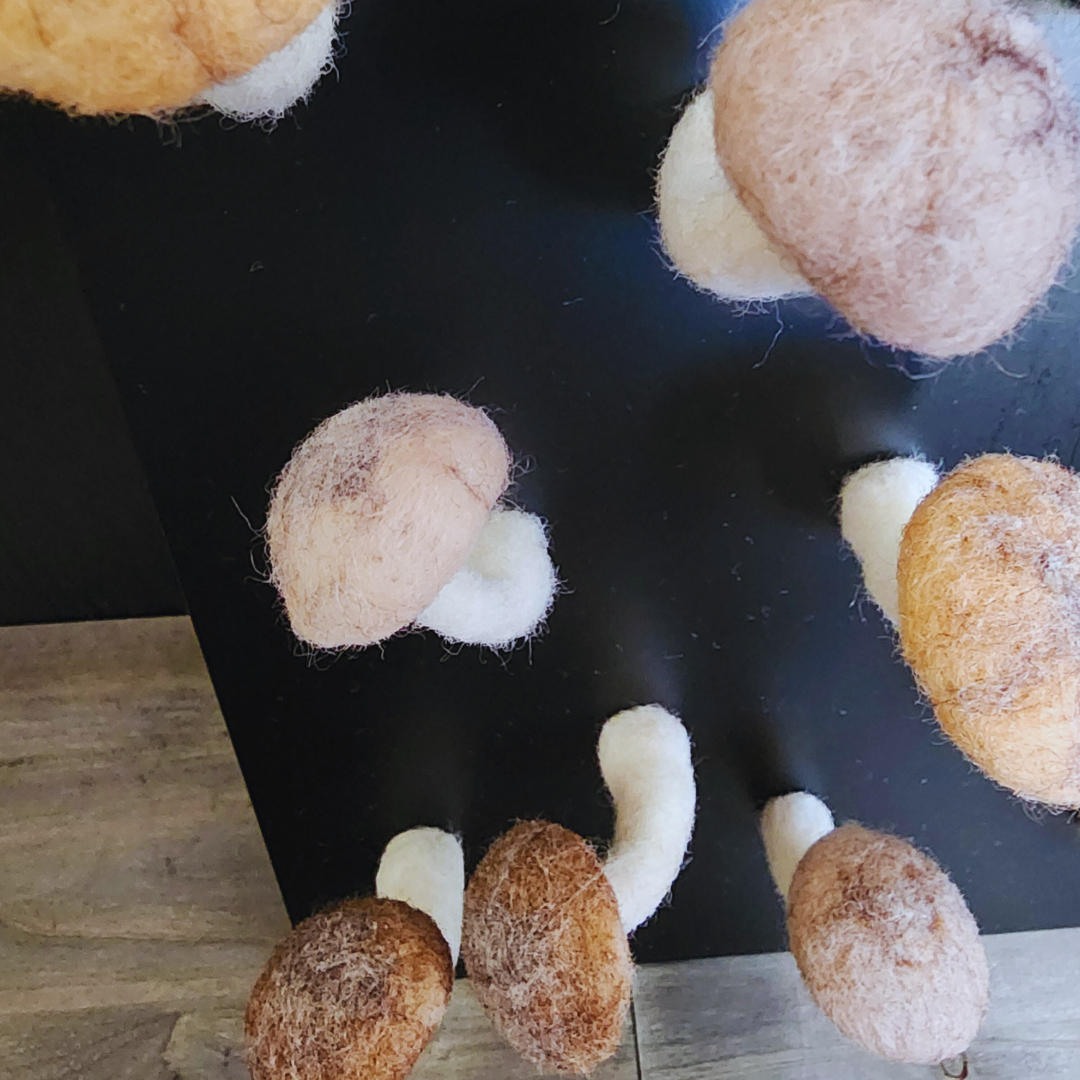 An angled close-up view of multiple handmade felted brown mushroom magnets with white stems, attached to a black magnetic surface, some partially visible.