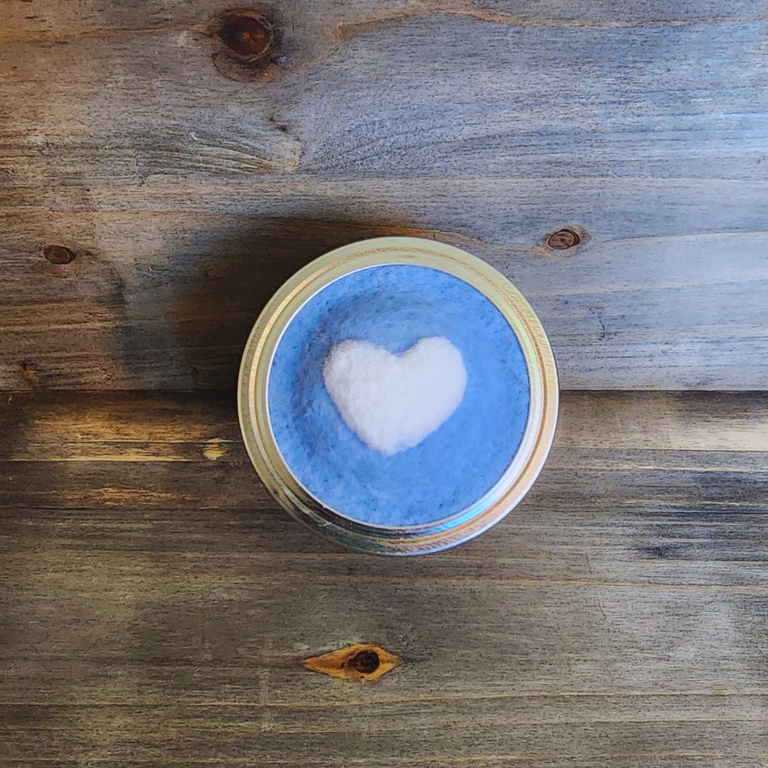A top-down shot of the blue and white heart pincushion lid against a rustic, dark-grained wooden background.