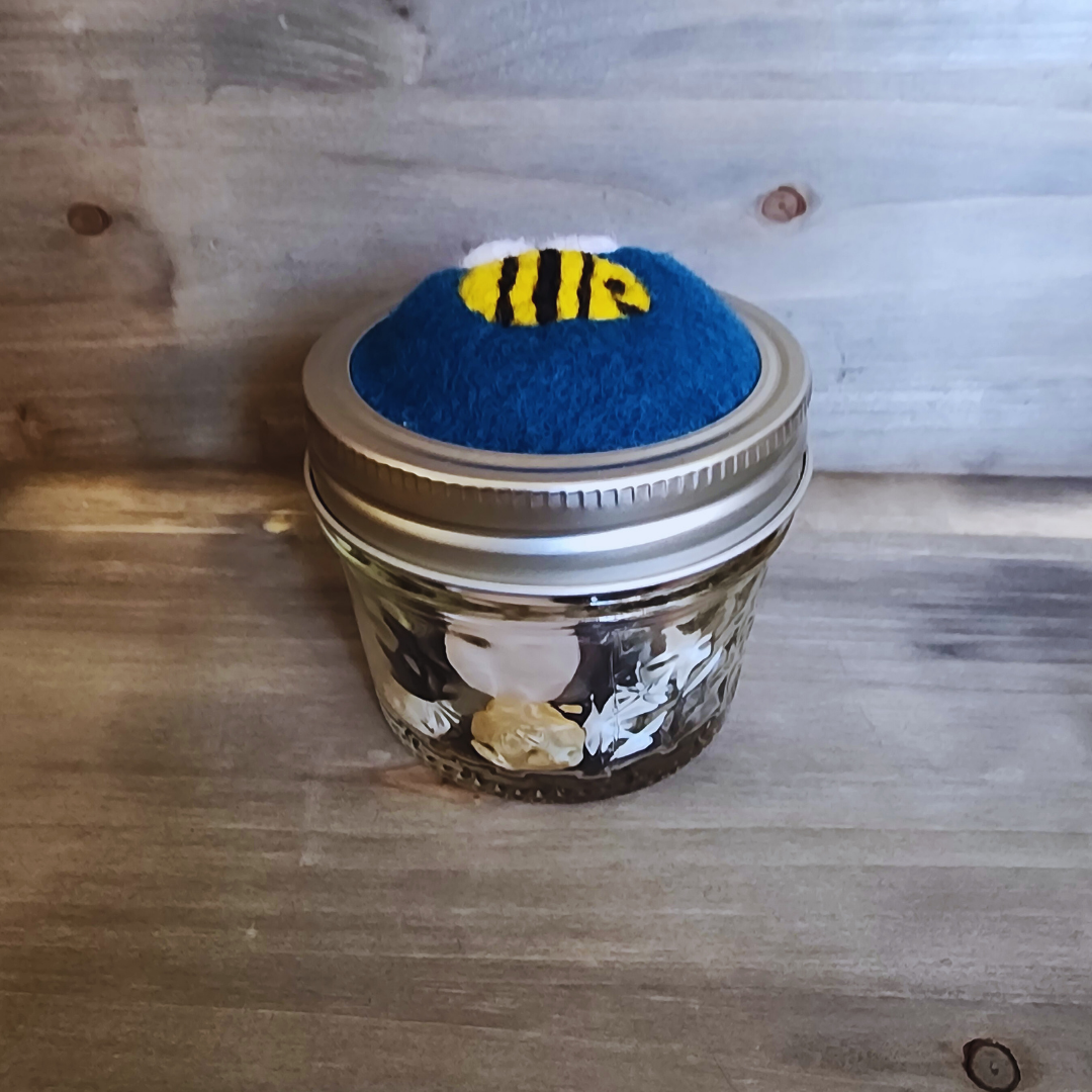 A side profile of the bumblebee jar emphasizing the domed blue wool topper and the collection of assorted neutral buttons stored inside the quilted glass.