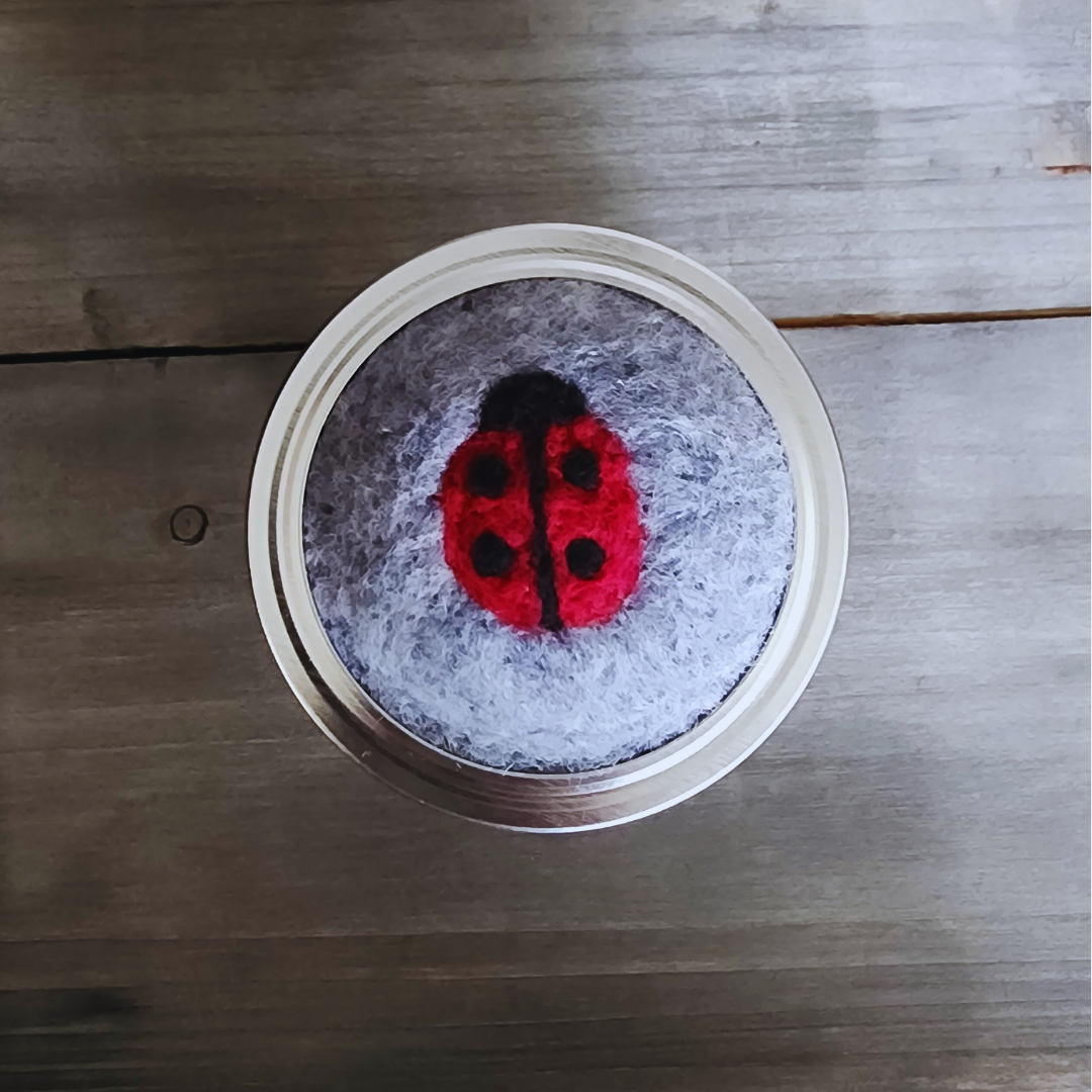 A direct top-down view of the gray needle-felted ladybug topper resting on a wooden surface.