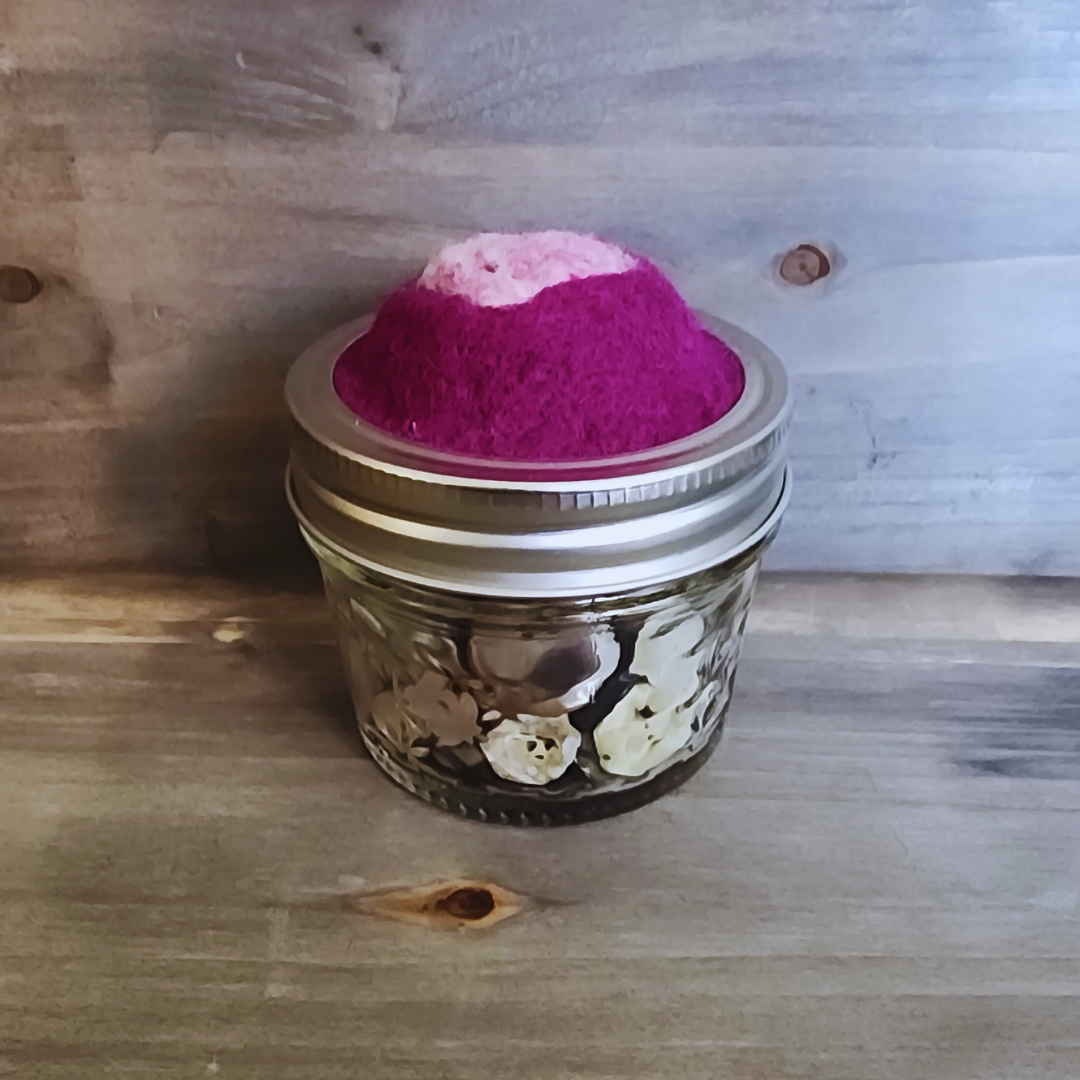 A side profile focusing on the domed magenta topper and the quilted glass jar filled with neutral-toned buttons.
