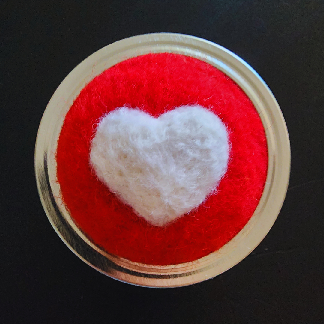 A top-down view of the bright red needle-felted base featuring a white 3D heart in the center.
