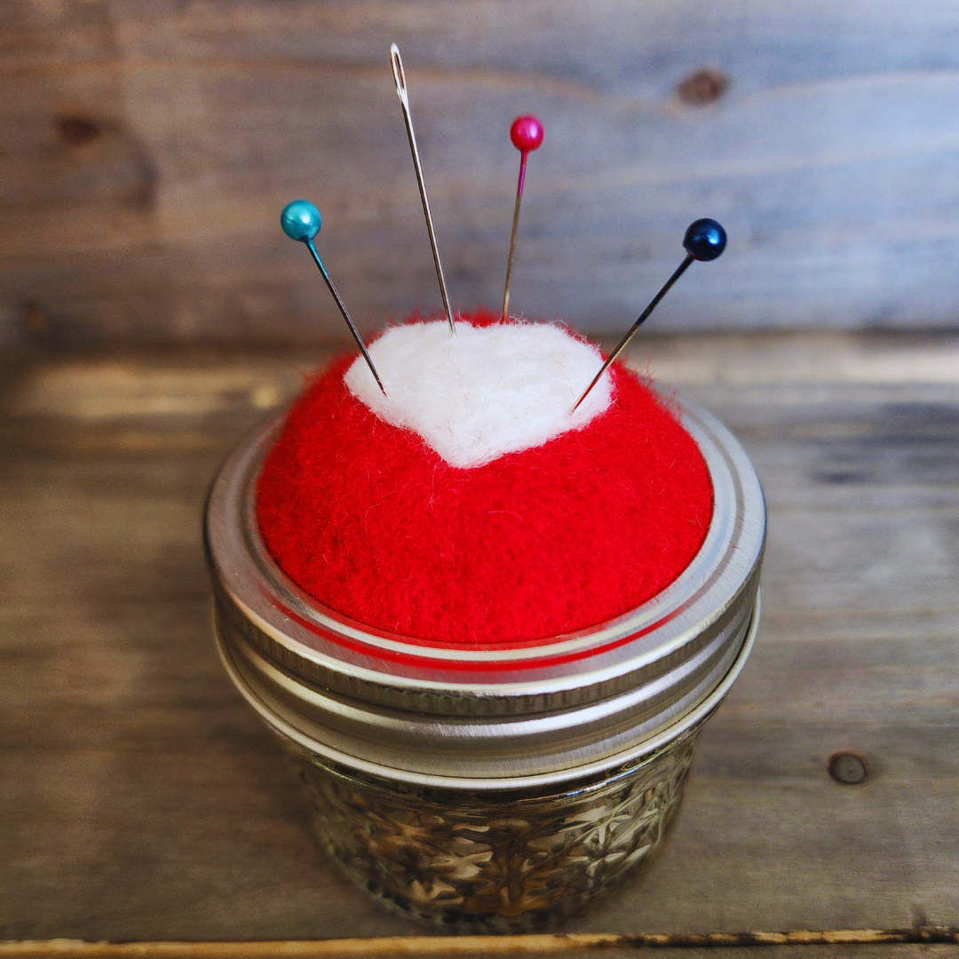 A side-angle shot of the red heart jar kit with teal, red, and dark blue pins inserted into the wool topper.