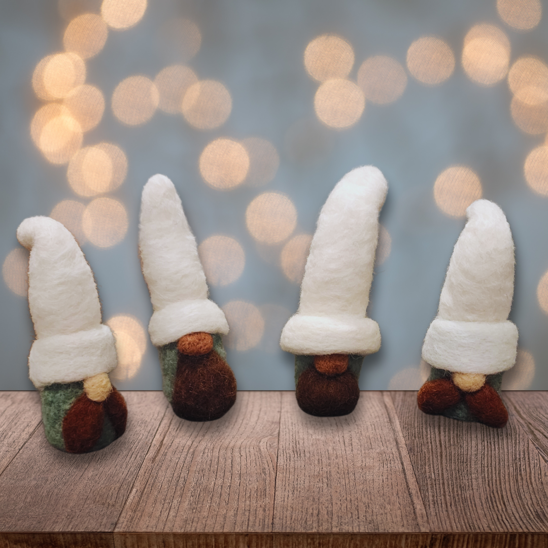 Four handmade needle-felted gnomes with aqua bodies and white hats, some with full brown beards and others with brown mustaches, standing on a wooden surface with blurred warm lights in the background.