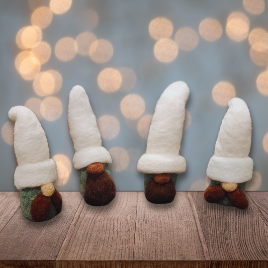 Four handmade needle-felted gnomes with aqua bodies and white hats, some with full brown beards and others with brown mustaches, standing on a wooden surface with blurred warm lights in the background.