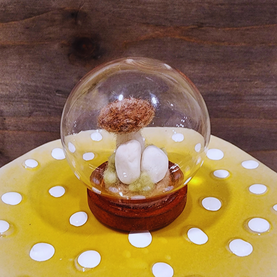 Close-up of a handmade felted Brown Cap mushroom terrarium in a glass globe, showing the white felt stones.
