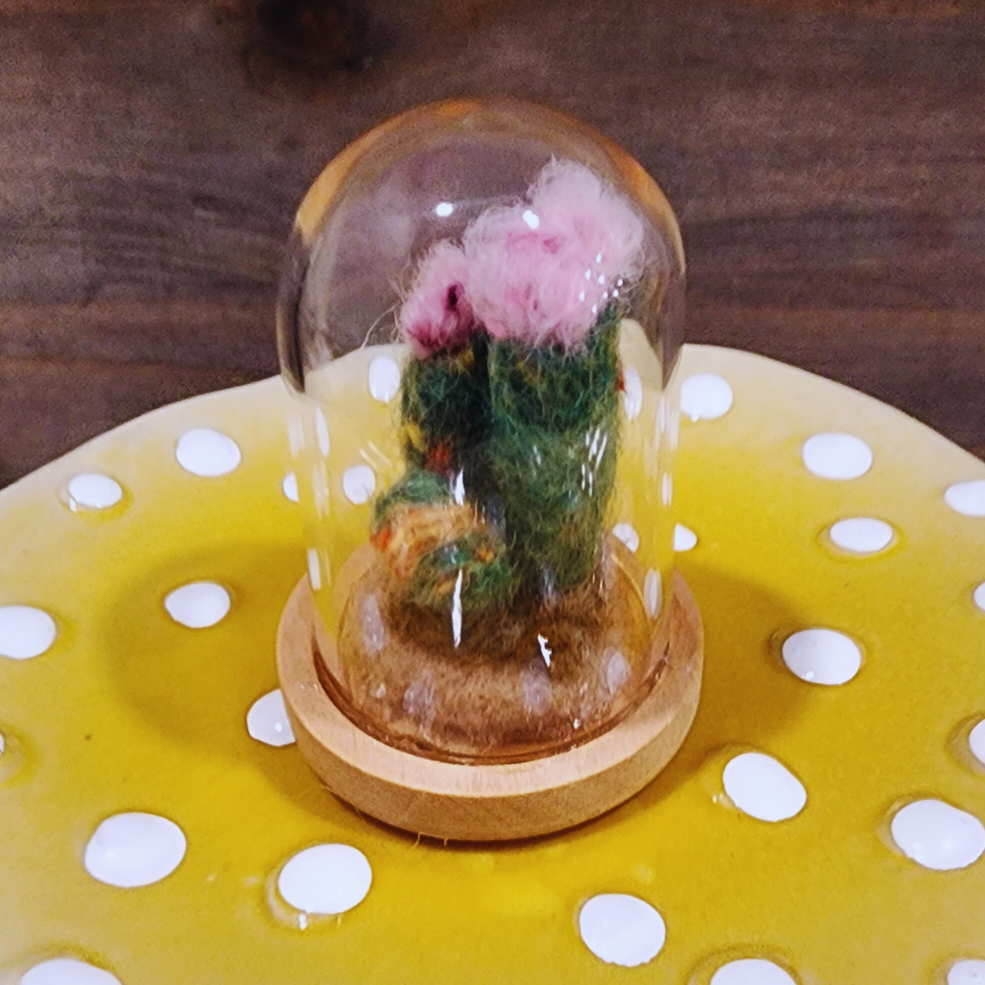 A handmade needle-felted Flowering Cactus terrarium with pink blooms, housed in a glass dome on a light wood base.