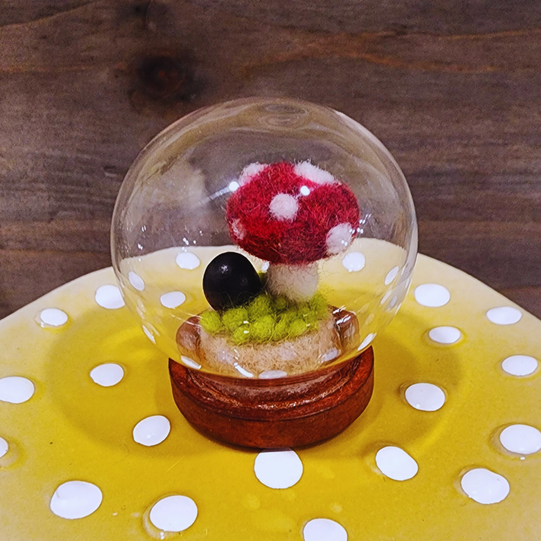 A handmade felted Toadstool mushroom terrarium in a glass globe, showing the felted moss base.