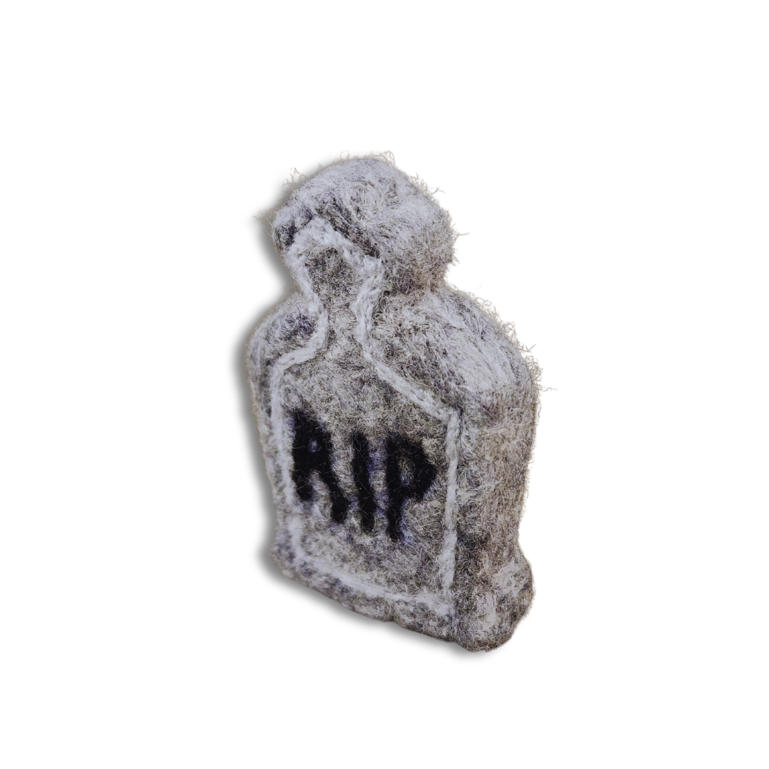 A handmade felted tombstone figurine in gray with a black "RIP" inscription, viewed from an angled perspective against a white background.