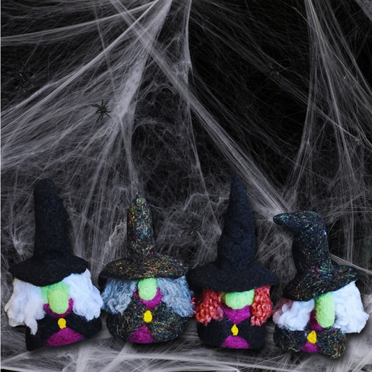 A group of four handmade needle-felted witch figurines with various hats, green faces, and different hair colors, standing in a row against a black and white spiderweb backdrop.