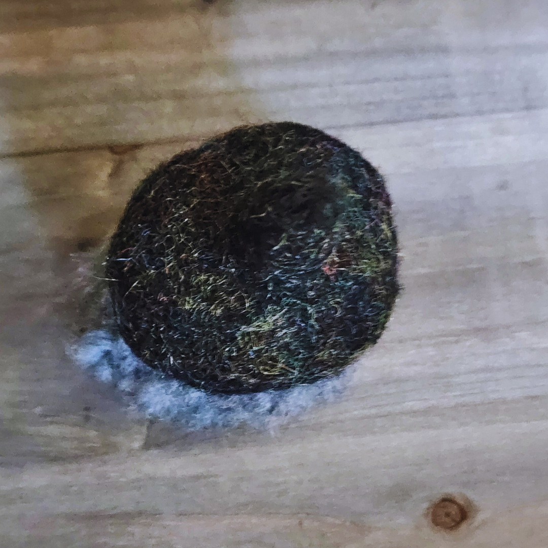 An overhead view of a handmade needle-felted witch figurine with a black sparkly pointy hat and fluffy grey hair, on a wooden background.