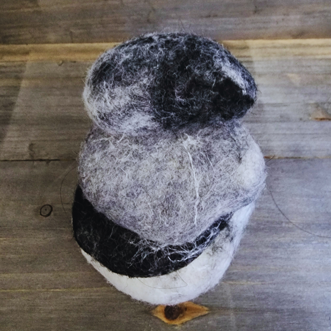 A close-up side view of three handmade wet-felted Zen Stones stacked, showing textures in white, black, and gray on a rustic wooden background.
