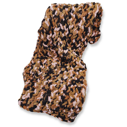 A handmade chunky knit blanket in a brown, pink, and black multicolor yarn, folded and viewed from above against a plain light gray background.
